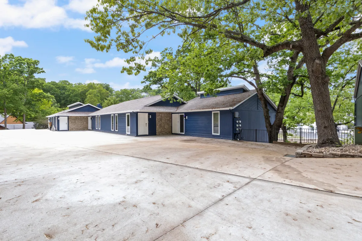 This exterior image showcases the blue facade of the building surrounded by large, mature trees and an open parking area. The scene hints at a welcoming environment where guests can gather outside, enjoy nature, and easily access their vehicles for exploring nearby attractions.