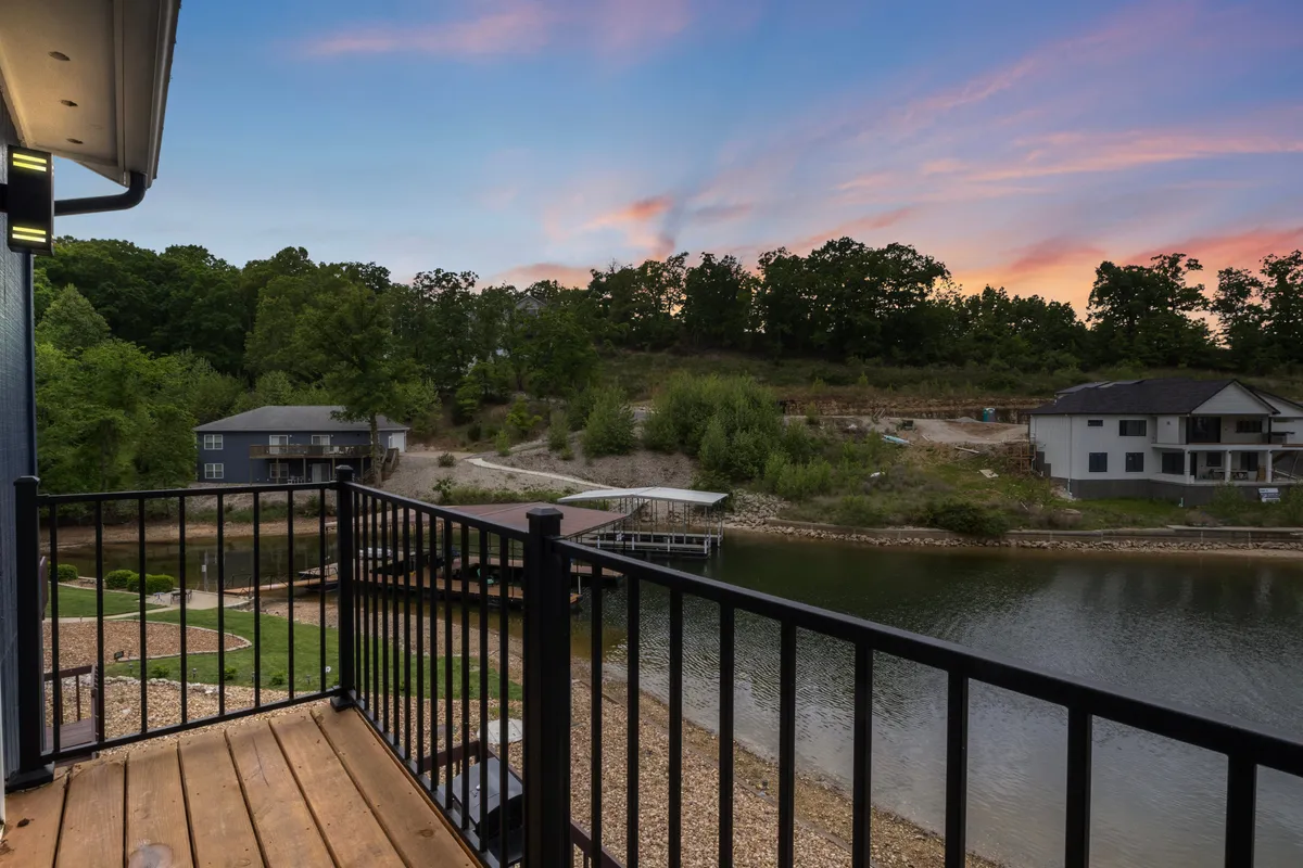 A balcony scene looking out over the water, with a railing in the foreground, distant trees, and sunset hues in the sky. The view suggests spaces for relaxation and social moments just steps away from the dock.