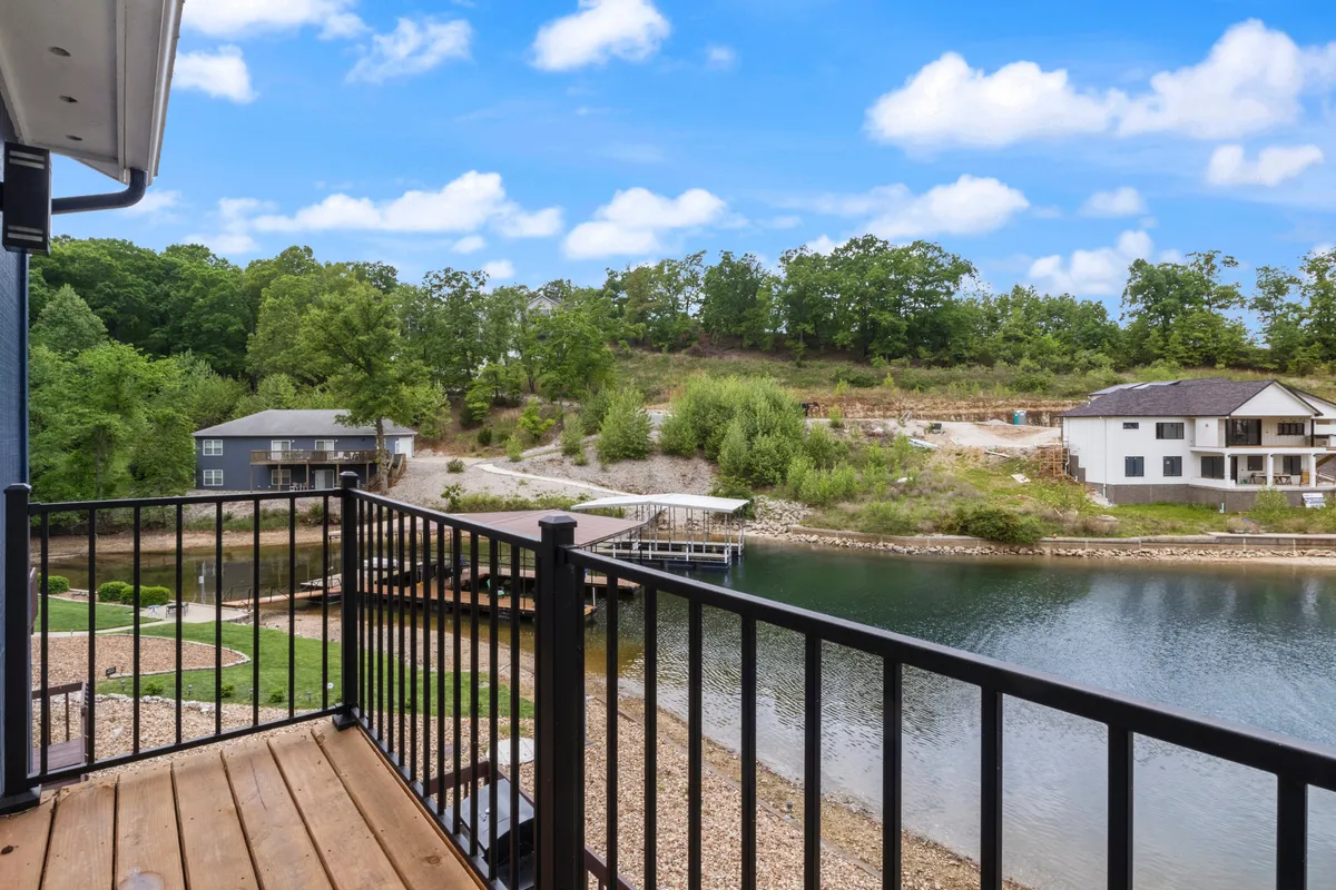 A peaceful view of the lake from a balcony, with a railing and green hillside visible. The setting evokes relaxation and enjoyment of the water, hinting at activities like swimming, fishing, and family gatherings by the shore.