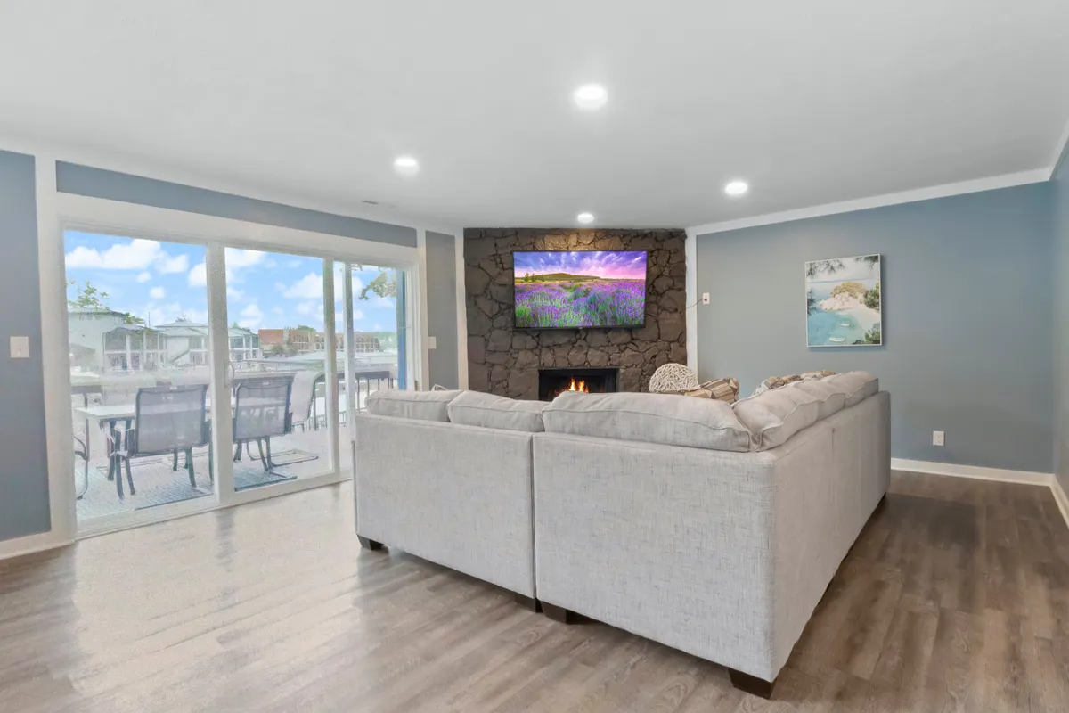 A spacious, welcoming living room featuring a large sectional sofa with plush cushions, a stone fireplace that anchors the space, a flat-screen TV, and sliding glass doors leading to the outdoors. The open, well-lit atmosphere is both relaxing and practical for families—including those traveling with pets—while the sectional and easy-to-clean surfaces support pet-friendly needs.