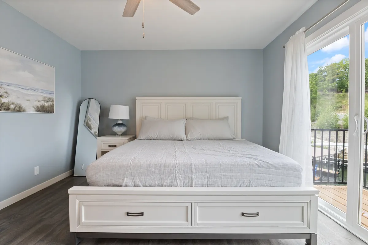 A cozy, restful bedroom with a comfortable bed, soothing artwork on the wall, a warm bedside lamp, and a window letting in soft morning light. The overall decor is clean, calm, and inviting, evoking a sense of peace and relaxation.